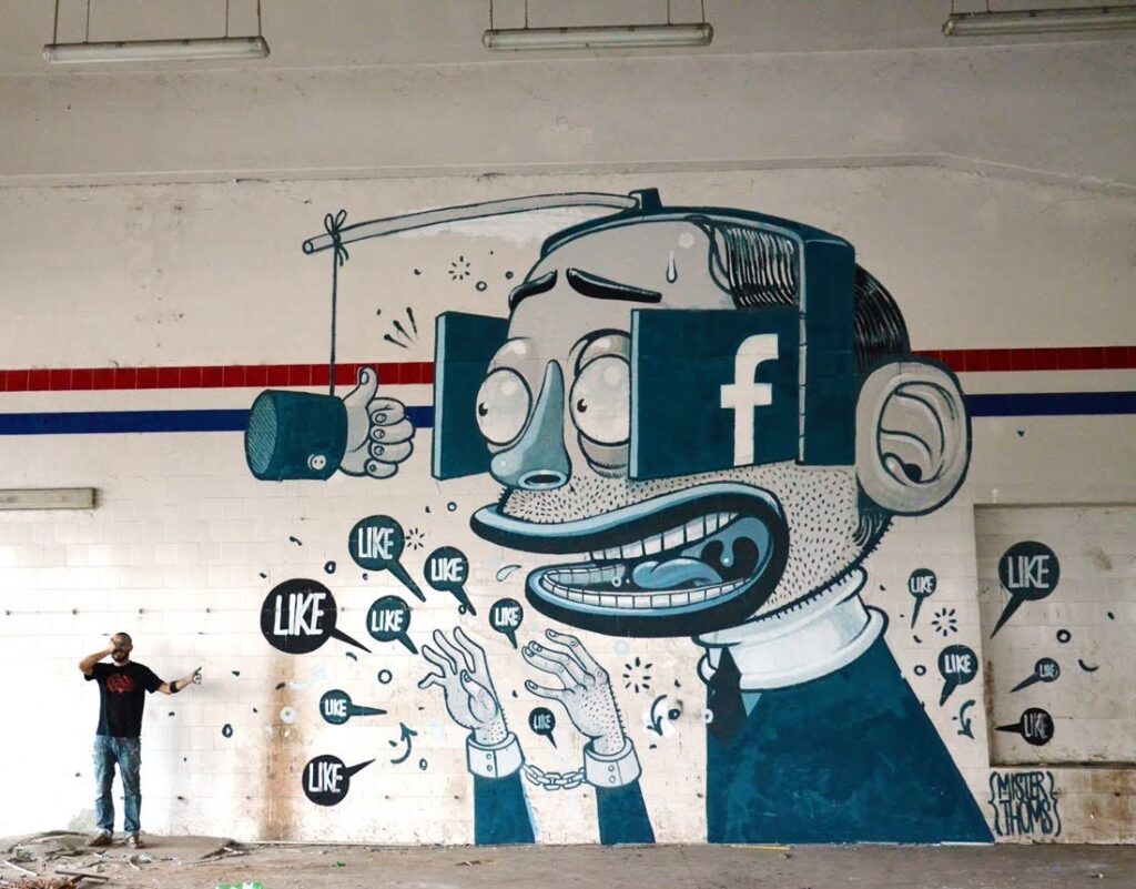 Tänagraffiti, kus suure suuga ja suurte kõrvadega mehel on peas Facebooki logoga silmaklapid ja tema pähe on kinnitatud õng, mille otsas ripub üles tõstetud pöial ta silmade kõrgusel. Itaalia tänavakunstniku Mister Thomsi töö „Like a Vision” Ferentinos. YouTube’i kuvatõmmis
